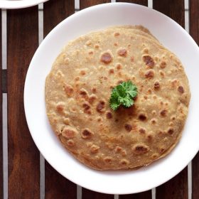 mooli paratha garnished with a coriander leaf and served on a white plate.