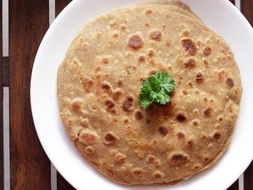 mooli paratha garnished with a coriander leaf and served on a white plate.
