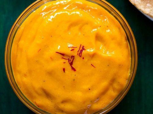 top shot of aamras in glass bowl with a few saffron strands on top on a green wooden tray