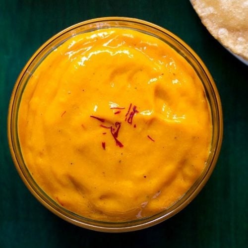 top shot of aamras in glass bowl with a few saffron strands on top on a green wooden tray