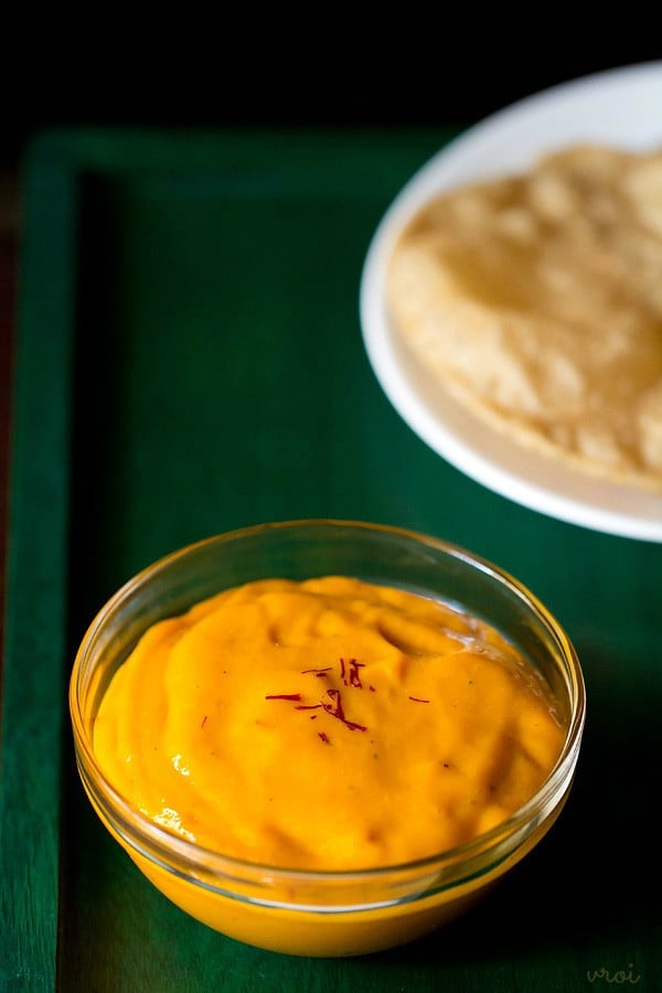 aamras in glass bowl with a few saffron strands on top on a green wooden tray