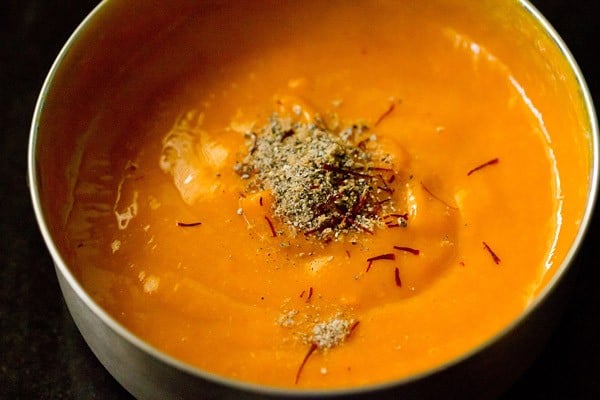 aamras in a steel bowl sprinkled with ground cardamom and saffron strands