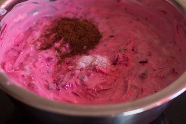 dark pink colored raita in bowl with a mound of cumin powder and salt