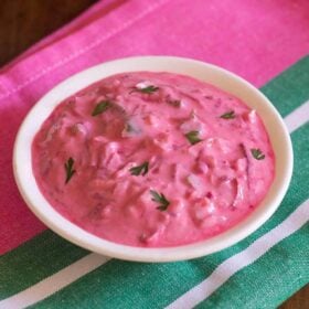 beetroot raita filled in white bowl on top of a dark pink and green colored folded cotton napkin