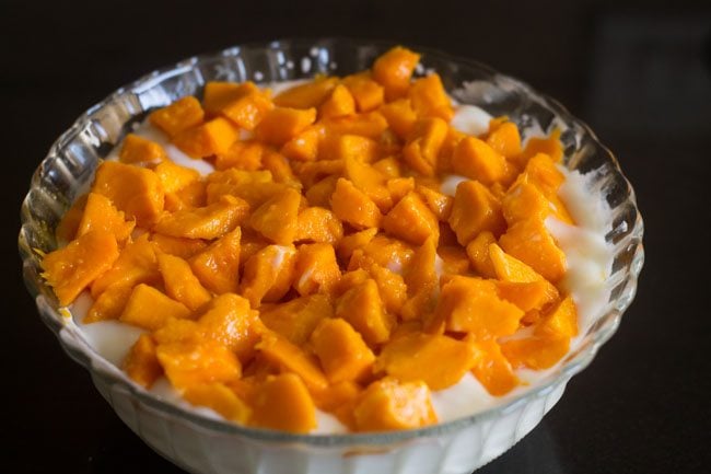 adding chopped mangoes to sweetened curd 