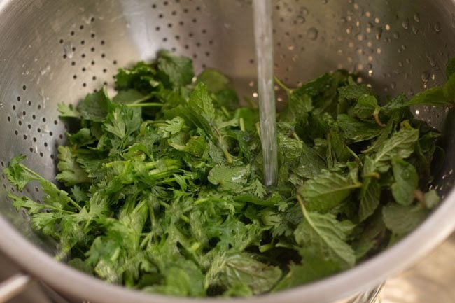 cilantro and mint being rinsed in a colander with water