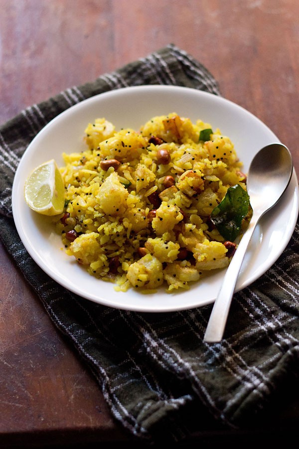 batata poha served on a white plate with a lemon wedge kept on the left side and a spoon kept on the right side.