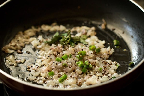 curry leaves and chopped green chilies added to onions for making batata poha.