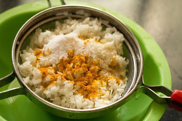 turmeric powder, sugar and salt added to rinsed flattened rice for making aloo poha.