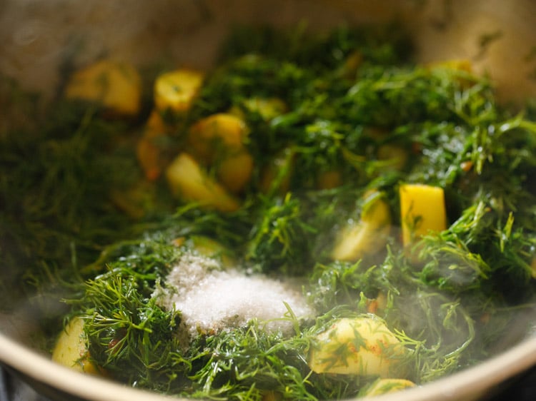 adding salt to dill leaves and potatoes mixture
