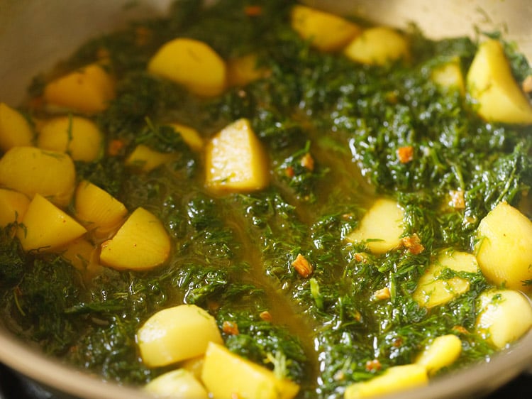 mixing water with dill leaves and potatoes in the kadai