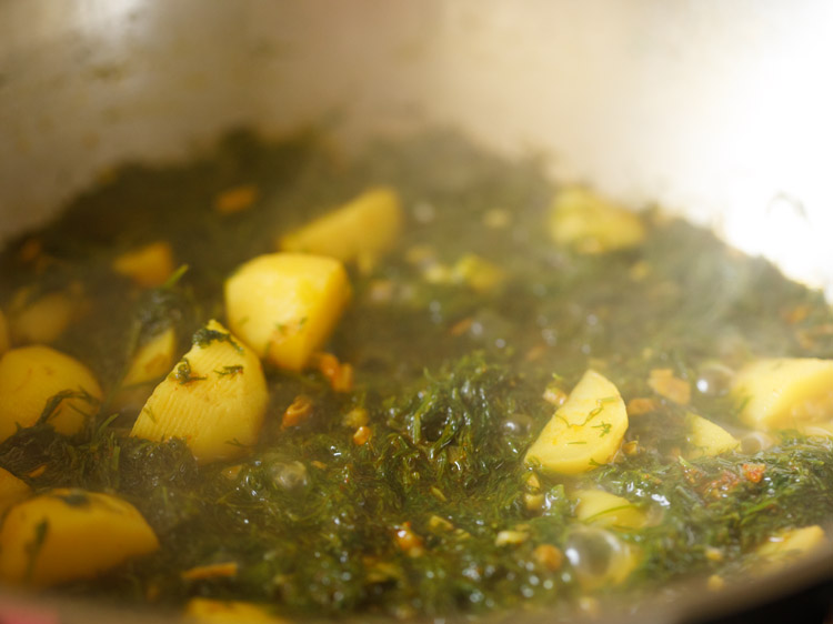 cooking dill leaves and potatoes in the kadai
