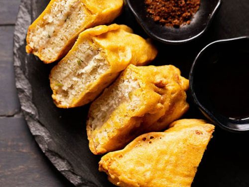 bread pakora triangles on a black round stone platter.