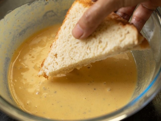 assembled bread with potato stuffing being dipped in besan batter