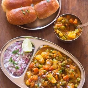 khada pav bhaji served in a plate with sides of pav and chopped onions, lemon wedges.