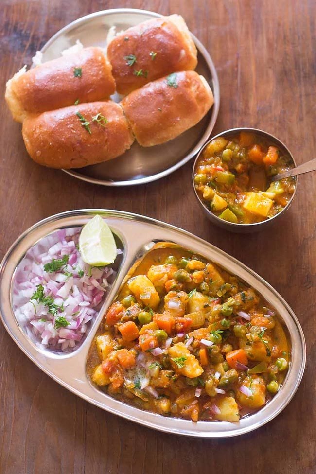 khada pav bhaji served in a plate with sides of pav and chopped onions, lemon wedges.