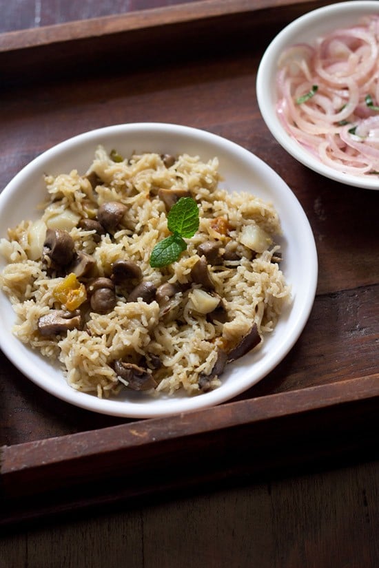 mushroom pulao served on a white plate with a side of sliced onions on a small white plate