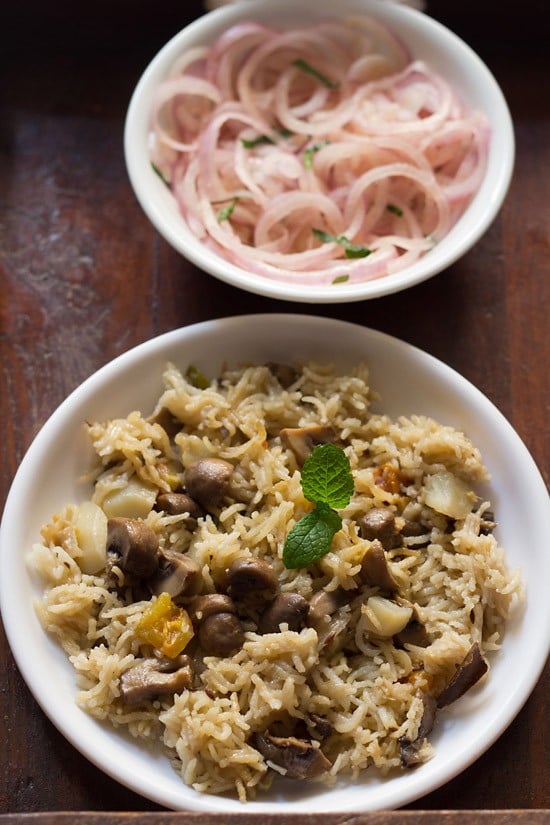 mushroom pulao served on a white plate with a side of sliced onions on a small white plate.