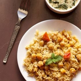 chana pulao served on a white plate with spinach raita.