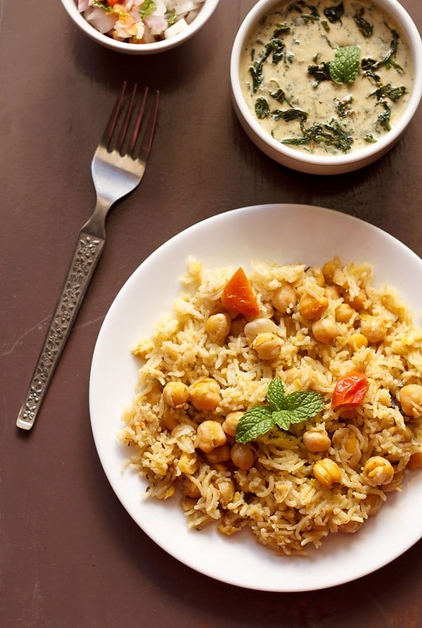 chana pulao served on a white plate with spinach raita.