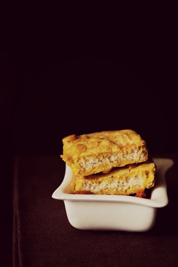 halved bread bajji on a bowl of tomato chutney