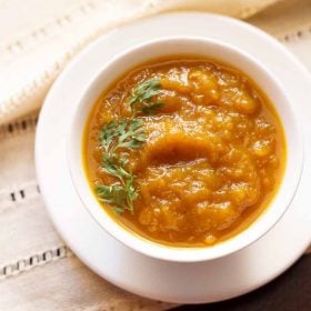 kaddu ki sabji garnished with coriander sprig and served in a white bowl placed on a white tray.