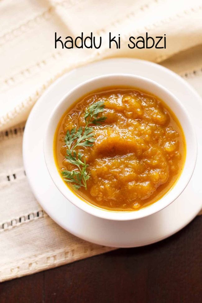 kaddu ki sabji garnished with coriander sprig and served in a white bowl placed on a white tray.