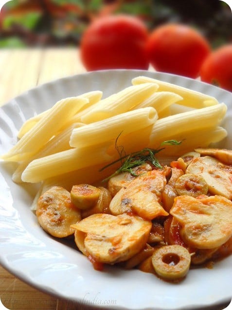 penne pasta with tomatoes and mushroom sauce on a white plate.