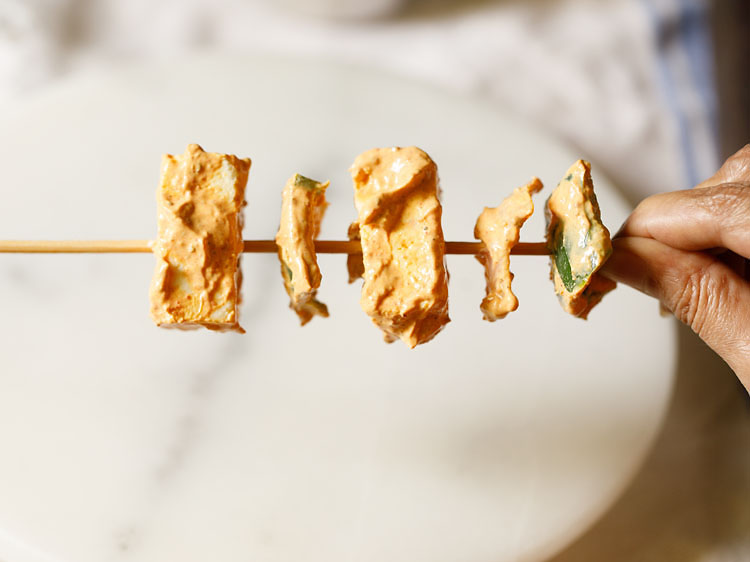 marinated paneer, onions and capsicum being threaded in bamboo skewers