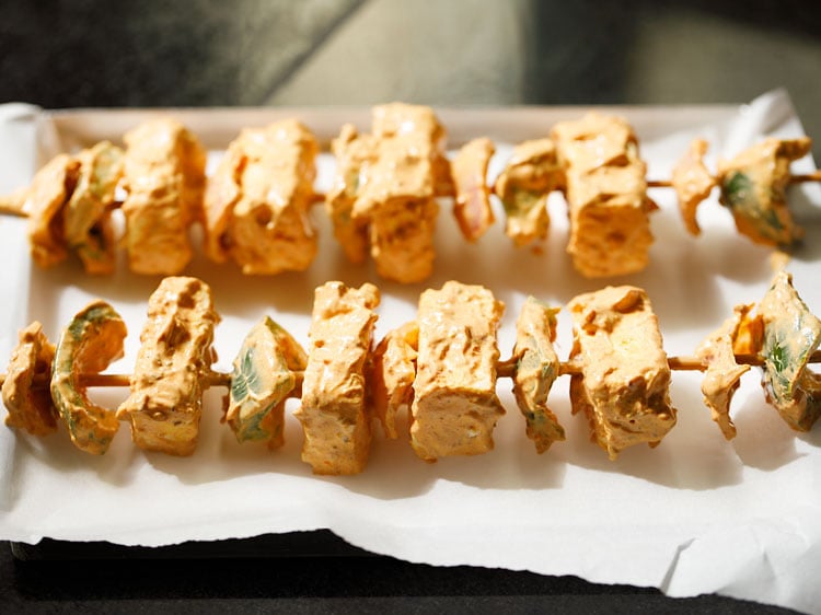 skewers with threaded paneer, onions and capsicum kept on parchment paper on a baking tray