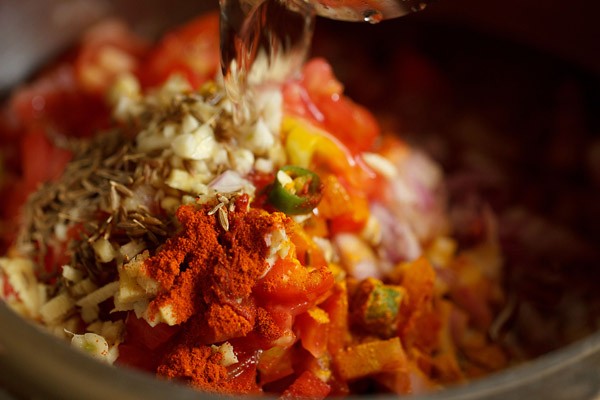 water being poured on top of the spices, herbs and veggies