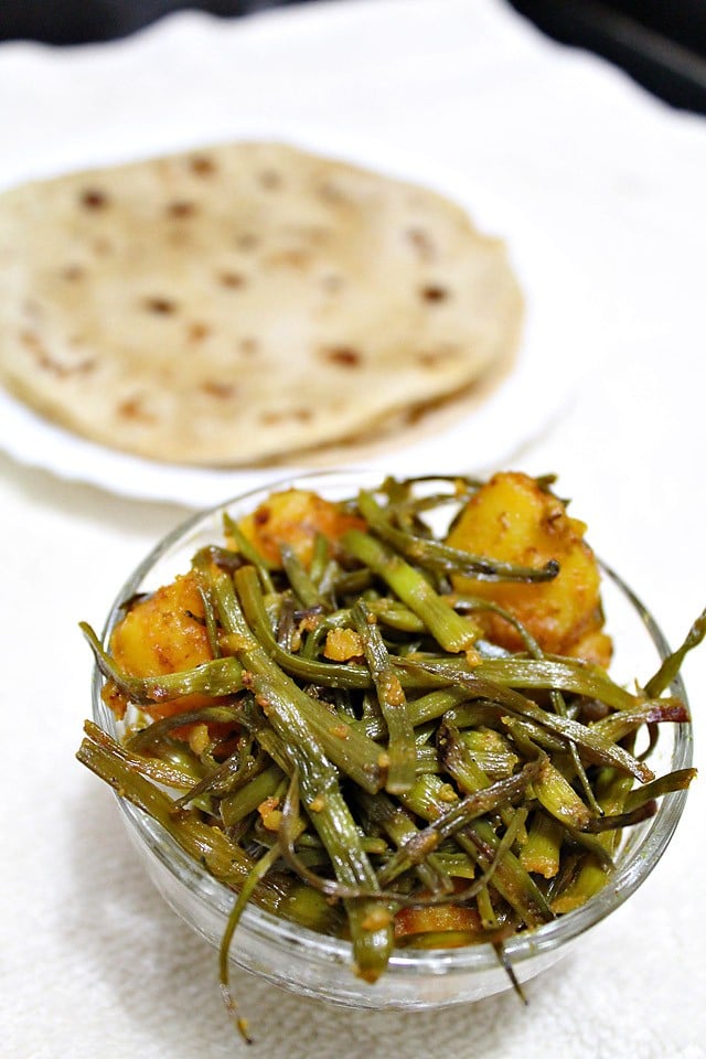aloo mogri ki sabzi served in a glass bowl with chapatis kept on a plate at the back. 