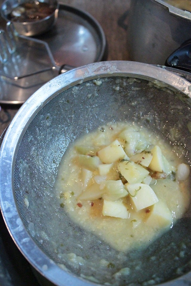 sieving the cooked vegetables and lentils through a strainer and mashing. 