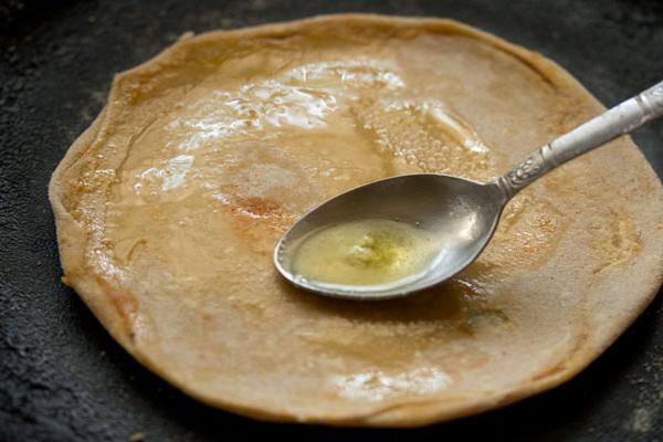 applying ghee on gobi paratha with a spoon