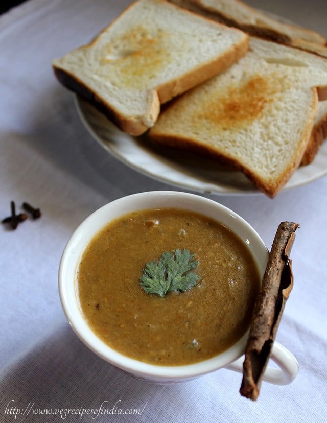 dhansak garnished with coriander leaves and served in a white bowl with toasted bread kept on a plate in the side.