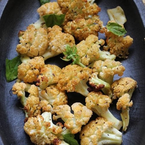 baked cauliflower on a dark grey-brown plate and garnished with fresh basil leaves.