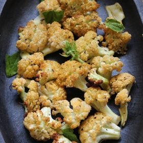 baked cauliflower on a dark grey-brown plate and garnished with fresh basil leaves.