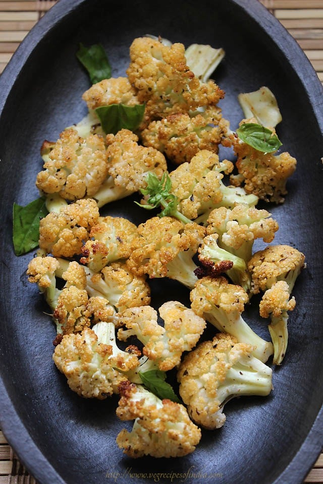 baked cauliflower on a dark grey-brown plate and garnished with fresh basil leaves.