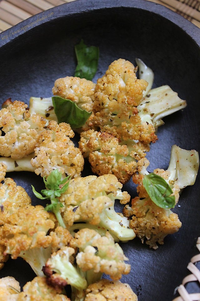 close up of baked cauliflower on a grey plate and garnished with fresh basil leaves.