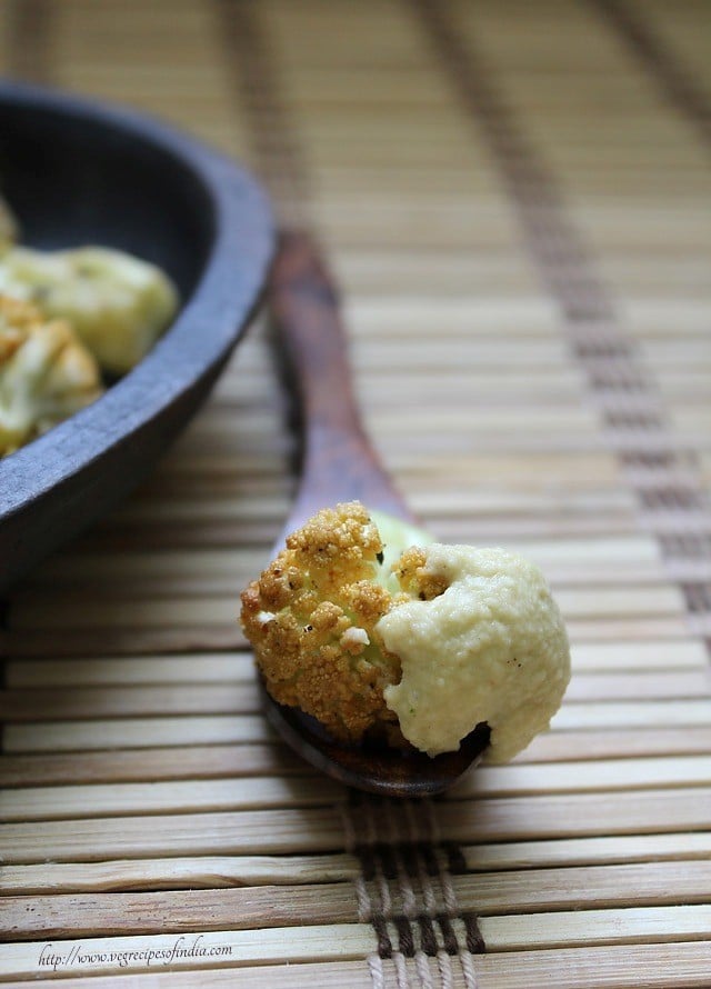 one floret of baked cauliflower on a spoon with hummus.