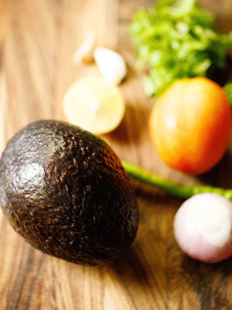 all the guacamole ingredients like avocado, onion, tomato etc on wooden chopping board.