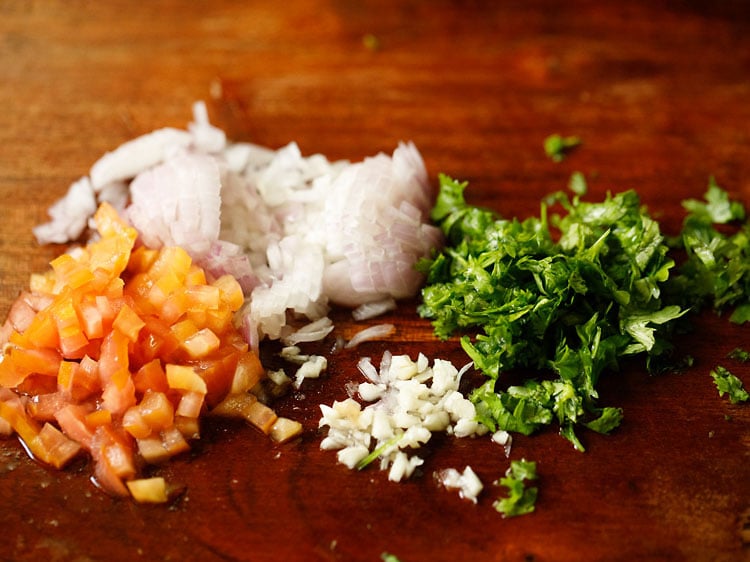 chopped onions, tomatoes, garlic, serrano peppers, & cilantro on a chopping board.