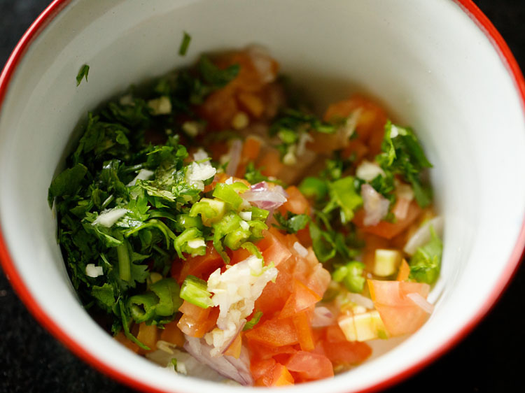 chopped onions, tomatoes, peppers, coriander leaves, garlic in a mixing bowl.
