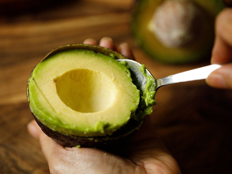 scooping avocado pulp with a spoon.