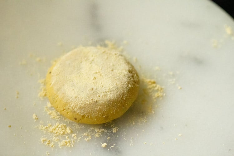 cornmeal sprinkled on flattened dough ball on white marble rolling board