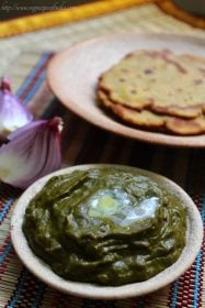 palak saag in a shallow clay bowl with melted butter on top. with makki ki roti kept on a plate in the background.