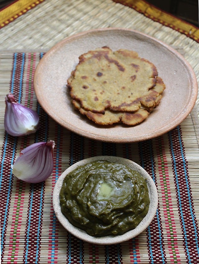 palak saag in a clay bowl with halved red onion by the side and cornmeal flatbreads placed on top in a clay plate.