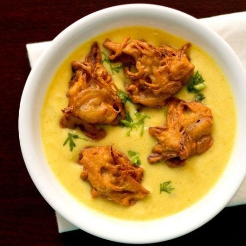 kadhi topped with pakora and coriander leaves in a white bowl.