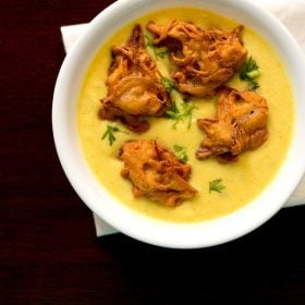 kadhi topped with pakora and coriander leaves served in a white bowl