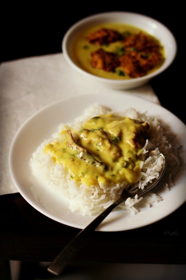 kadhi pakora served over a bed of steamed rice on a white plate with a spoon on the rice 